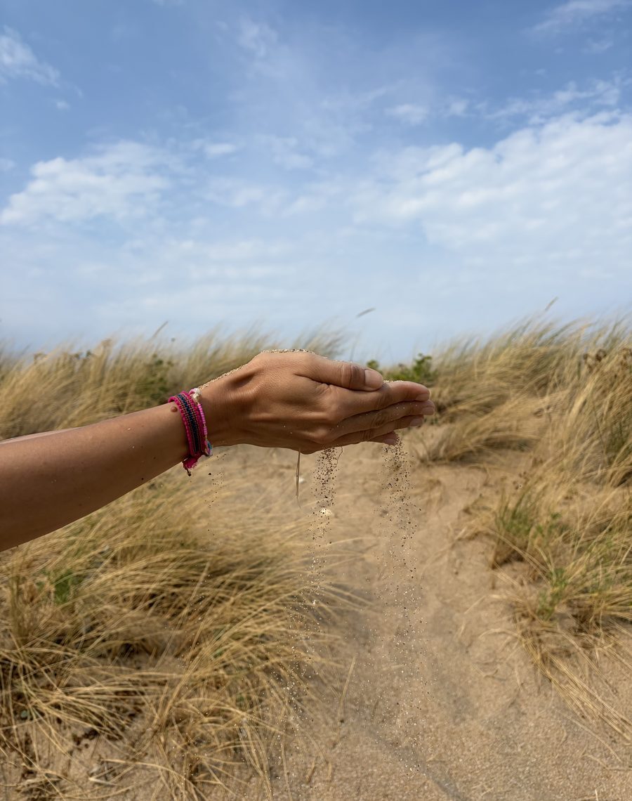 Sable qui coule entre les mains, dans les herbes hautes sous un grand ciel bleu
